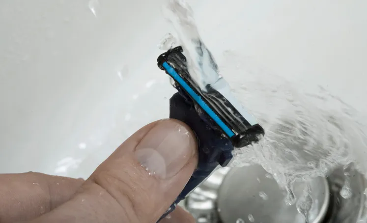 Mão segurando lâmina de barbear embaixo da torneira aberta